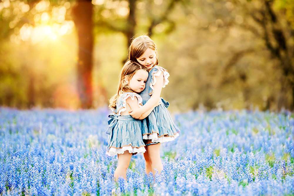 two little girls hugging in bluebonnet field in texas hill country